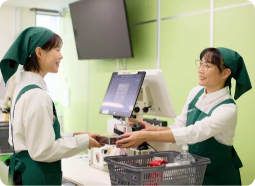 主婦スタッフのI.T.さんが研修スタッフにレジ操作を教えている様子